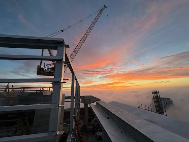 partner Structural steel framing and a construction crane against a sunset sky